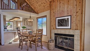 A spacious dining area with a wooden table and chairs, a fireplace, and a large window providing a view of the outdoors. - Panoramic Views From This Monthly Rental in Cambria! Stunning! (Cambria)