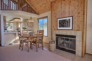 A spacious dining area with a wooden table and chairs, a fireplace, and a large window providing a view of the outdoors. - Panoramic Views From This Monthly Rental in Cambria! Stunning! (Cambria)