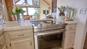 A kitchen with a stainless steel oven, white cabinets, and a large window providing a view of the outdoors. - Panoramic Views From This Monthly Rental in Cambria! Stunning! (Cambria)
