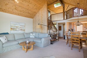 A spacious living area with a light grey sofa, a wooden coffee table, and a dining table with chairs. A staircase leads to an upper level. - Panoramic Views From This Monthly Rental in Cambria! Stunning! (Cambria)
