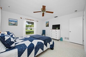 A bedroom with a bed, a ceiling fan, a window with curtains, a desk with a computer, and a door. - Spacious 3 Bedroom 2 Bath Walk to Eagle Lake Park Fenced Yard (Clearwater)