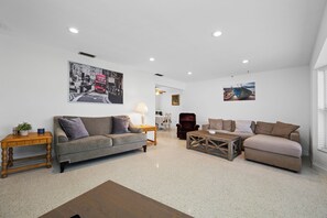A spacious living room with a grey sofa, a wooden coffee table, and a red armchair. There are two wall-mounted paintings and a ceiling light fixture. - Spacious 3 Bedroom 2 Bath Walk to Eagle Lake Park Fenced Yard (Clearwater)
