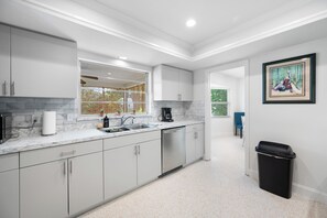 Una cocina moderna con armarios blancos, encimera de mármol y un bote de basura negro.