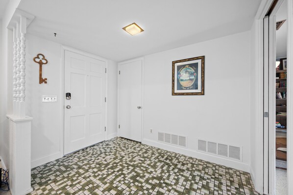 Un pasillo con suelo estampado, puertas blancas, una llave en la pared y un cuadro enmarcado.