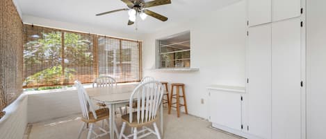 Quarto com mesa de jantar, cadeiras, ventoinha no teto, janela com persianas e guarda-roupa branco.