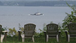 En vy över en vattenyta med en båt i fjärran, omgiven av grönska och några trästolar.