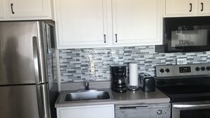 A kitchen with stainless steel appliances, white cabinets, a tiled backsplash, and a coffee maker. - 'Slopeside Escape' Mtn Lodge; Looking Directly at Ballhooter!! (Snowshoe)