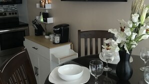 A dining area with a table set for two, a vase of white flowers, and a framed picture of a snowy landscape on the wall. - 'Slopeside Escape' Mtn Lodge; Looking Directly at Ballhooter!! (Snowshoe)