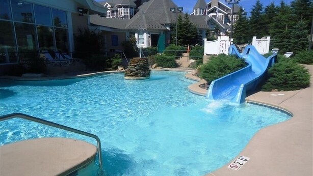 A swimming pool with a blue slide, surrounded by lounge chairs and a building with a turreted roof. - 'Slopeside Escape' Mtn Lodge; Looking Directly at Ballhooter!! (Snowshoe)