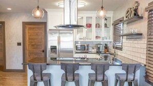 Een moderne keuken met roestvrijstalen apparatuur, een centraal kookeiland met barkrukken en een decoratieve wandplank.