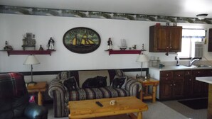 Una sala de estar con sofá, una mesa de centro de madera y una zona de cocina con armarios y fregadero.