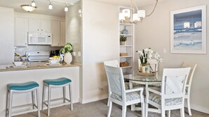 Une cuisine moderne avec des meubles blancs, un four à micro-ondes et un coin repas comprenant une table en verre et des chaises blanches.