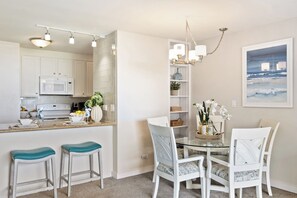 Een moderne keuken met witte kasten, een magnetron en een eethoek met een glazen tafel en witte stoelen.