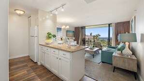 A modern kitchen with white cabinets, a wooden countertop, and a dining area with a green sofa and a table. - 2Bedroom w Ocean Views in BeachFront Resort - Kaanapali Shores 527 (Lahaina)