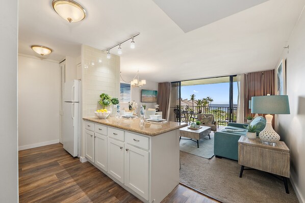 A modern kitchen with white cabinets, a wooden countertop, and a dining area with a green sofa and a table. - 2Bedroom w Ocean Views in BeachFront Resort - Kaanapali Shores 527 (Lahaina)