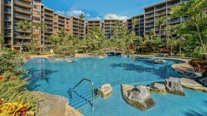 A hotel with multiple balconies, a swimming pool with rocks, and palm trees. - 2Bedroom w Ocean Views in BeachFront Resort - Kaanapali Shores 527 (Lahaina)