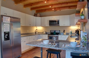 A modern kitchen with white cabinets, stainless steel appliances, granite countertops, and a wooden ceiling.