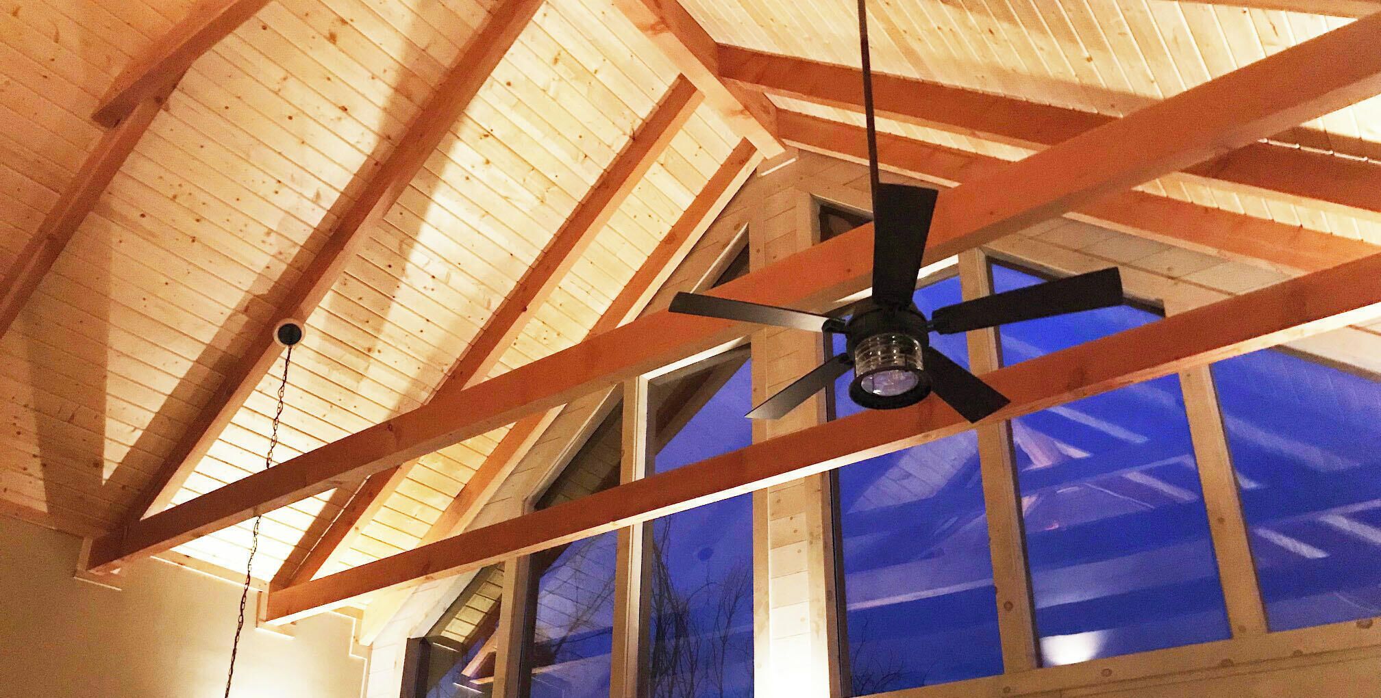 Ein Zimmer mit Holzbalken, einem Deckenventilator und großen Fenstern mit Blick zum Himmel.