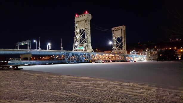 Vista nocturna de un puente con dos torres, un túnel bajo la carretera y suelo cubierto de nieve.