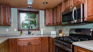 Una cocina con gabinetes de madera, un microondas de acero inoxidable, una estufa a gas y un salpicadero de azulejos.