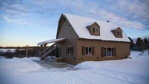 Una casa de madera de dos pisos con un porche cubierto y un techo cubierto de nieve.