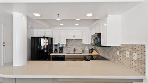 Una cocina moderna con armarios blancos, una isla grande con taburetes de bar, un refrigerador negro y un microondas.