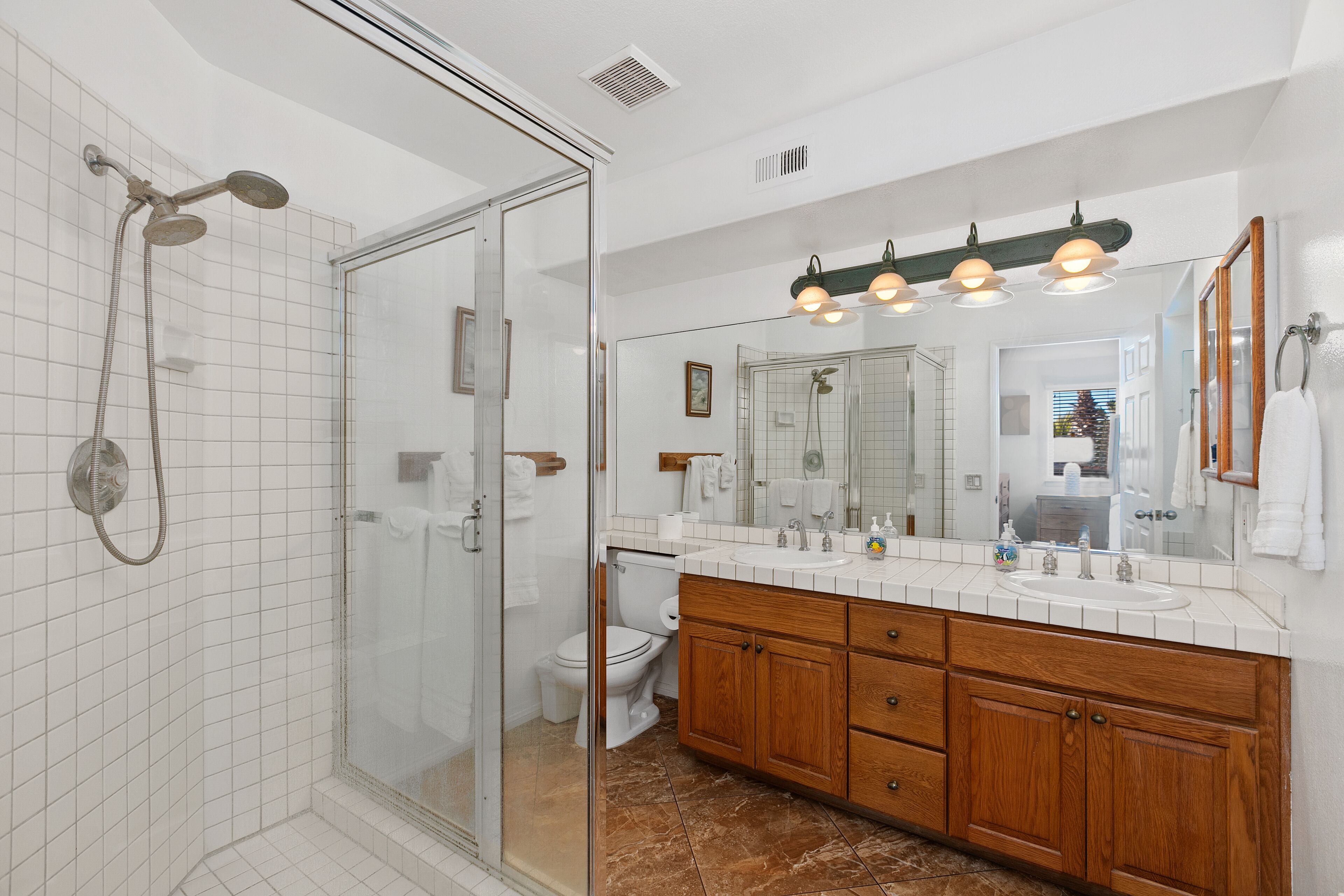 Une salle de bain moderne avec une douche à parois de verre, un meuble-lavabo en bois doté d’un grand miroir et un sol carrelé de couleur blanche.