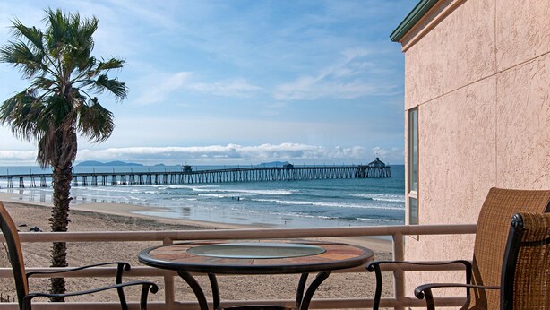 Vista de playa con una palmera, un muelle y una mesa con sillas.