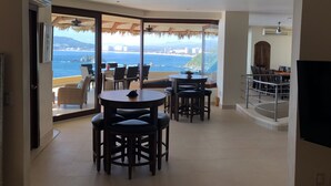 A spacious balcony with a view of the sea and mountains, furnished with a round table and chairs, and a dining area with a high table and chairs. - 3,400 sqft OCEANFRONT 3 BDR 4 BTR AMAZING CONDO. 900SQFT TERRACE STUNNING VIEWS (Ixtapa)