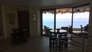 A spacious room with a balcony overlooking the sea, featuring a dining area with chairs and a table, and a staircase leading to the upper floor. - 3,400 sqft OCEANFRONT 3 BDR 4 BTR AMAZING CONDO. 900SQFT TERRACE STUNNING VIEWS (Ixtapa)
