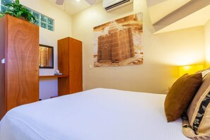 Une chambre d’hôtel avec un lit, une armoire en bois, un climatiseur fixé au mur et un tableau encadré.