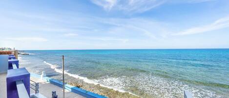 Vista costera con cielo despejado, costa rocosa y barandilla azul.