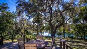 A wooden deck with a round table and four chairs, surrounded by trees and a view of a body of water. - Somewhere... for Birding and Boating (Dunnellon)