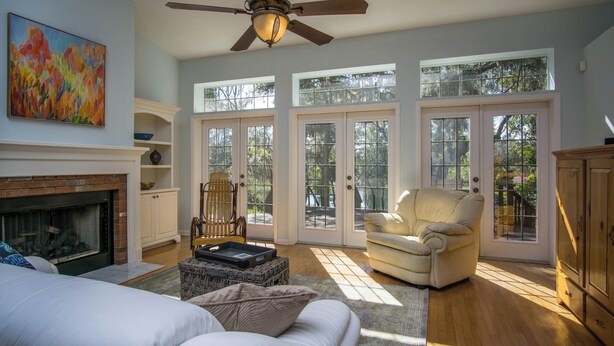 A spacious living room with a fireplace, a ceiling fan, and large windows. - Somewhere... for Birding and Boating (Dunnellon)