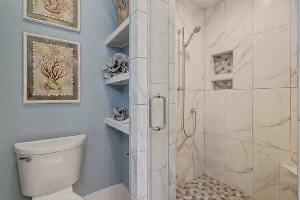 A bathroom with a toilet, a shower with a glass door, and two framed artworks on the wall.