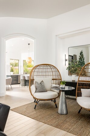 A modern living room with wicker chairs, a round coffee table, and a large mirror. - SWSS 3BR Kierland Indoor-Outdoor Desert Living | Heated Pool, Hot Tub, Fire Pit & 30‑Day Minimum (Scottsdale)
