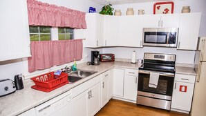 Uma cozinha compacta com armários brancos, micro-ondas de aço inoxidável, forno preto e escorredor de louça vermelho.