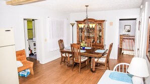 Uma área de refeições com uma mesa e cadeiras de madeira, um lustre e um armário de madeira com portas de vidro.