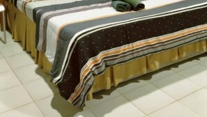 A single bed with a striped bedspread and pillows, a bedside table, and an air conditioning unit on the wall. - Guestroom Langkawi (Langkawi)