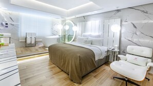 A modern hotel room with a large bed, a vanity with a mirror, a white armchair, and a small side table. - Chao Motel (Taoyuan City)