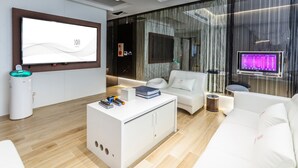 A modern hotel lobby with a reception desk, a white sofa, a massage chair, and a large digital screen displaying text. - Chao Motel (Taoyuan City)
