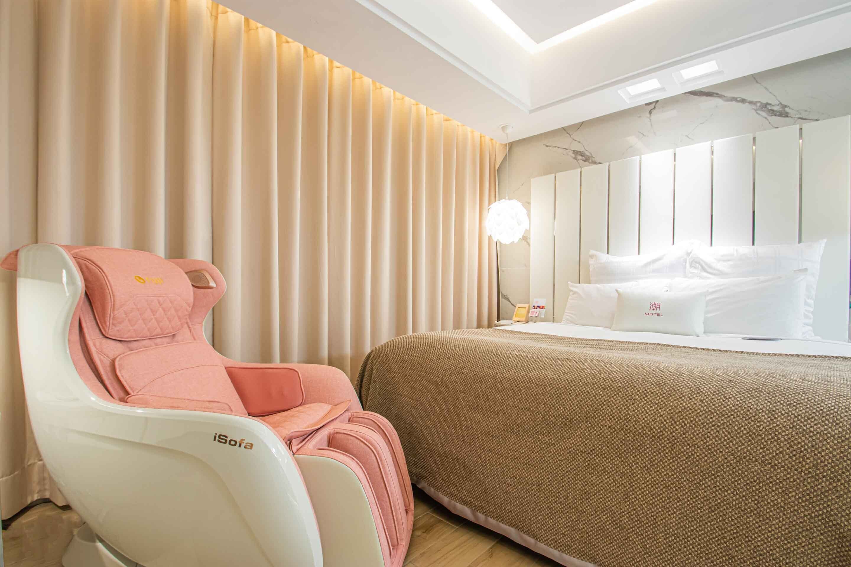 A hotel room with a massage chair, a bed with white bedding, and a marble-patterned wall.