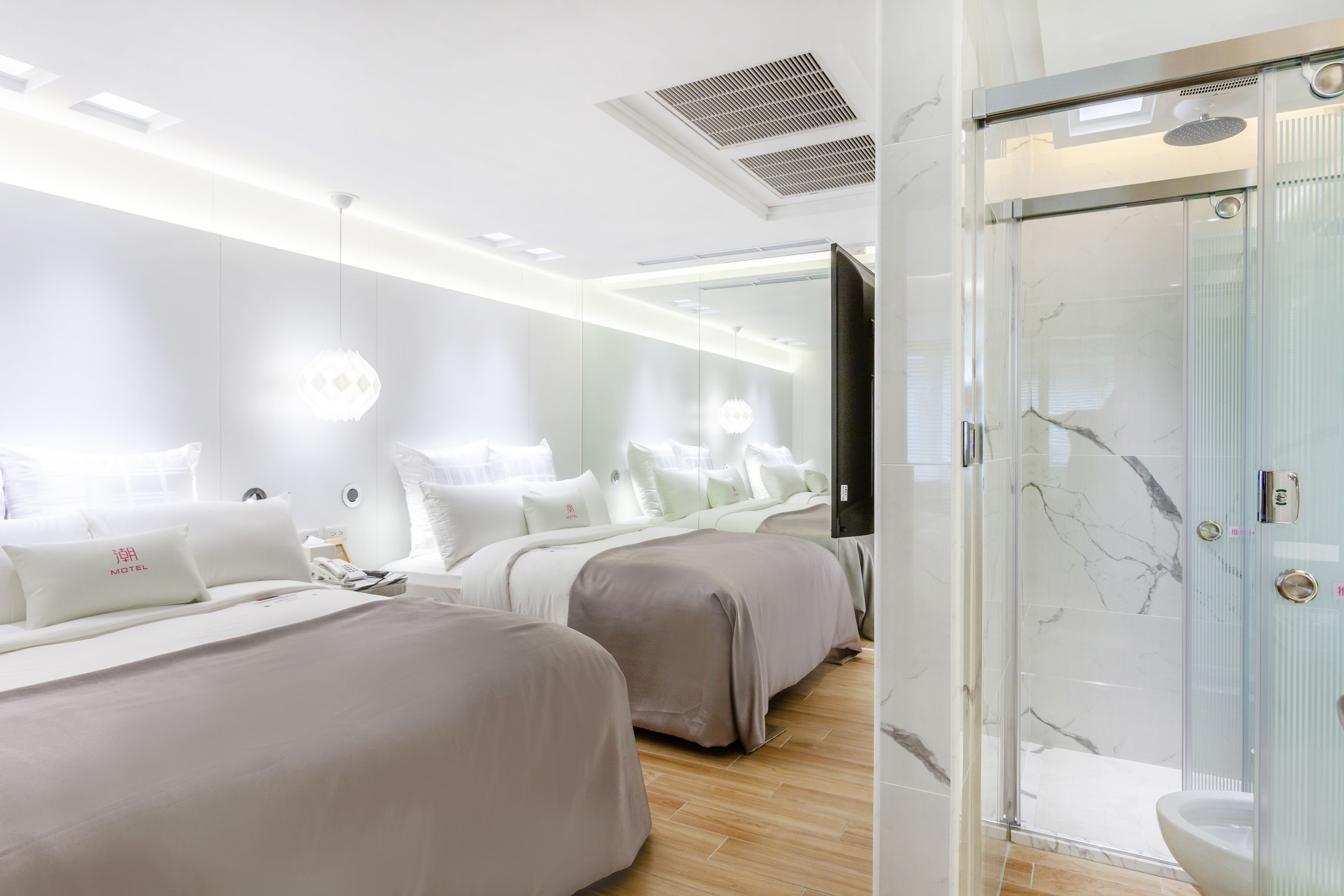A modern hotel room with a glass shower enclosure, a large mirror, and a bed with a headboard.