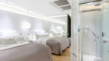 A modern hotel room with a glass shower enclosure, a large mirror, and a bed with a headboard.