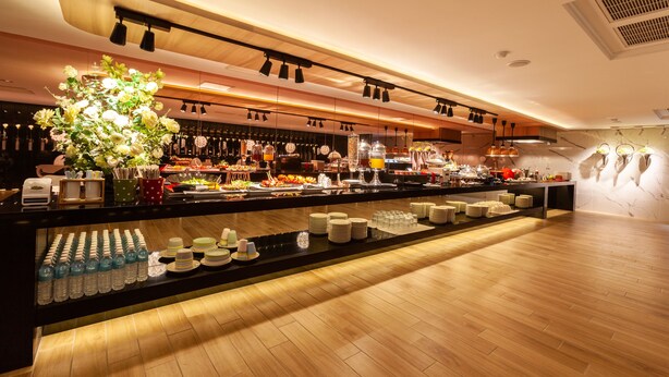 A modern hotel bar with a long counter, various food and drink options, and a decorative plant centerpiece. - Chao Motel (Taoyuan City)