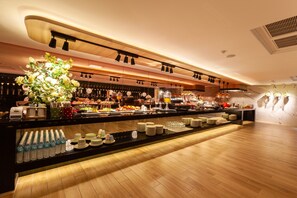 A modern hotel bar with a long counter, various food and drink options, and a decorative plant centerpiece. - Chao Motel (Taoyuan City)