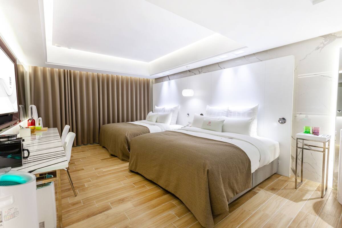 A hotel room with two beds, a dining table, a microwave, and a small table with glasses.