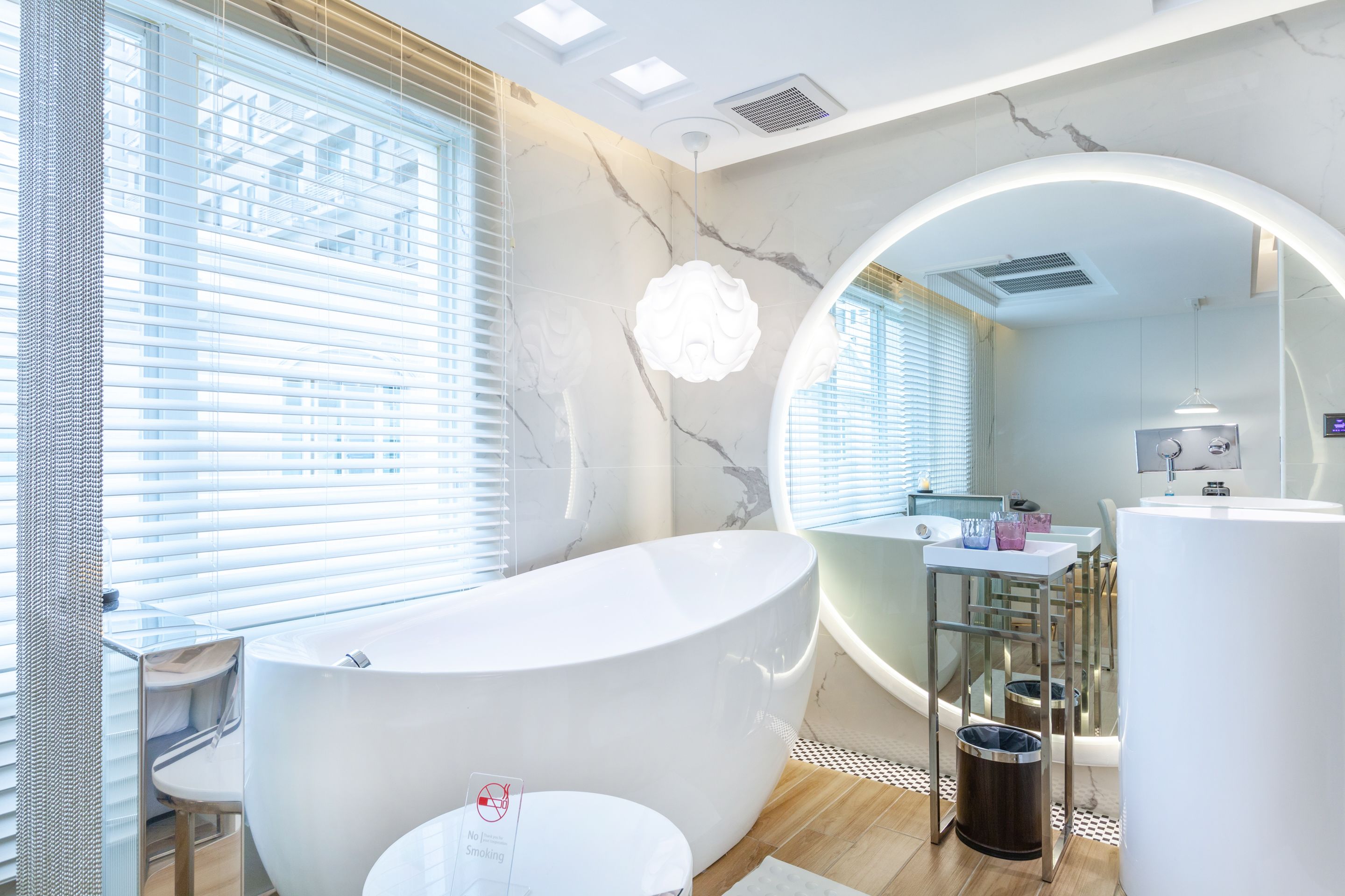 Een moderne badkamer met een vrijstaand bad, een wastafel met een spiegel en een ronde spiegel boven de wasbak.