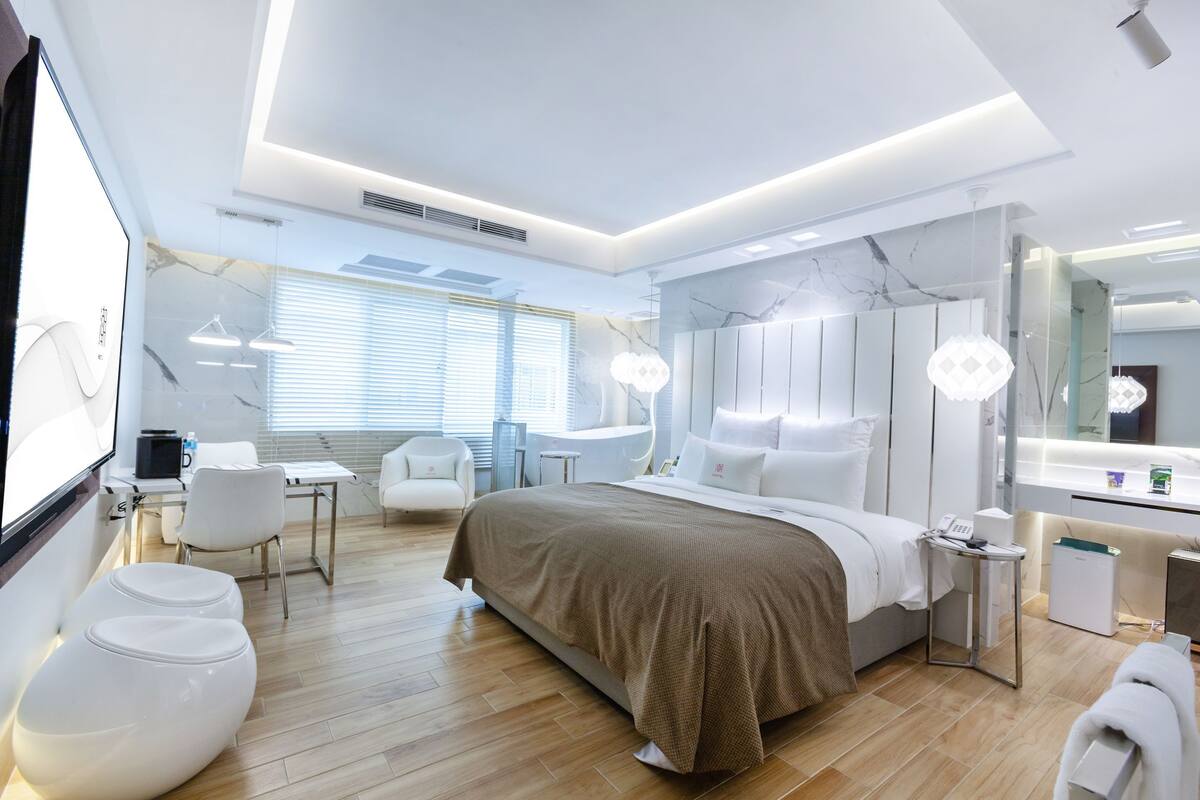 A modern hotel room with a large bed, bedside tables, a desk, a chair, and a bathroom area.