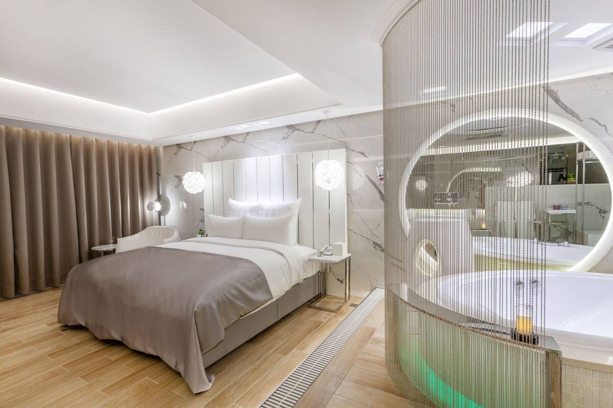 A modern bedroom with a large bed, a vanity with a mirror, and a circular jacuzzi tub.